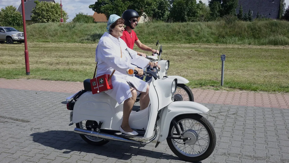 Frau in Gemeindeschwester-Uniform auf einem Moped: Die Kultfigur